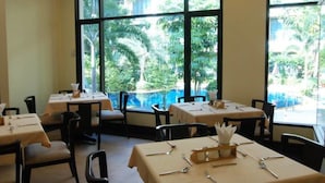 A restaurant with tables set for dining, large windows with a view of greenery and a pool. - Lecasa Bangsaen Hotel (Chonburi)