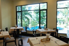 A restaurant with tables set for dining, large windows with a view of greenery and a pool.