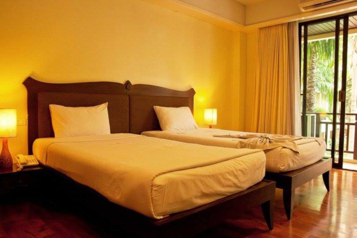 A hotel room with two beds, a wooden headboard, and a balcony with curtains.