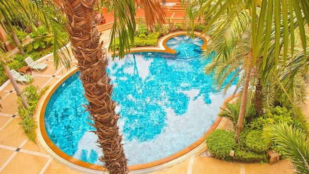 A circular pool surrounded by palm trees and greenery, with lounge chairs and a tiled floor. - Lecasa Bangsaen Hotel (Chonburi)