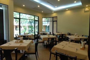 Zona pranzo con tavoli apparecchiati per gli ospiti, ampie finestre che lasciano entrare luce naturale e vista sul verde circostante.