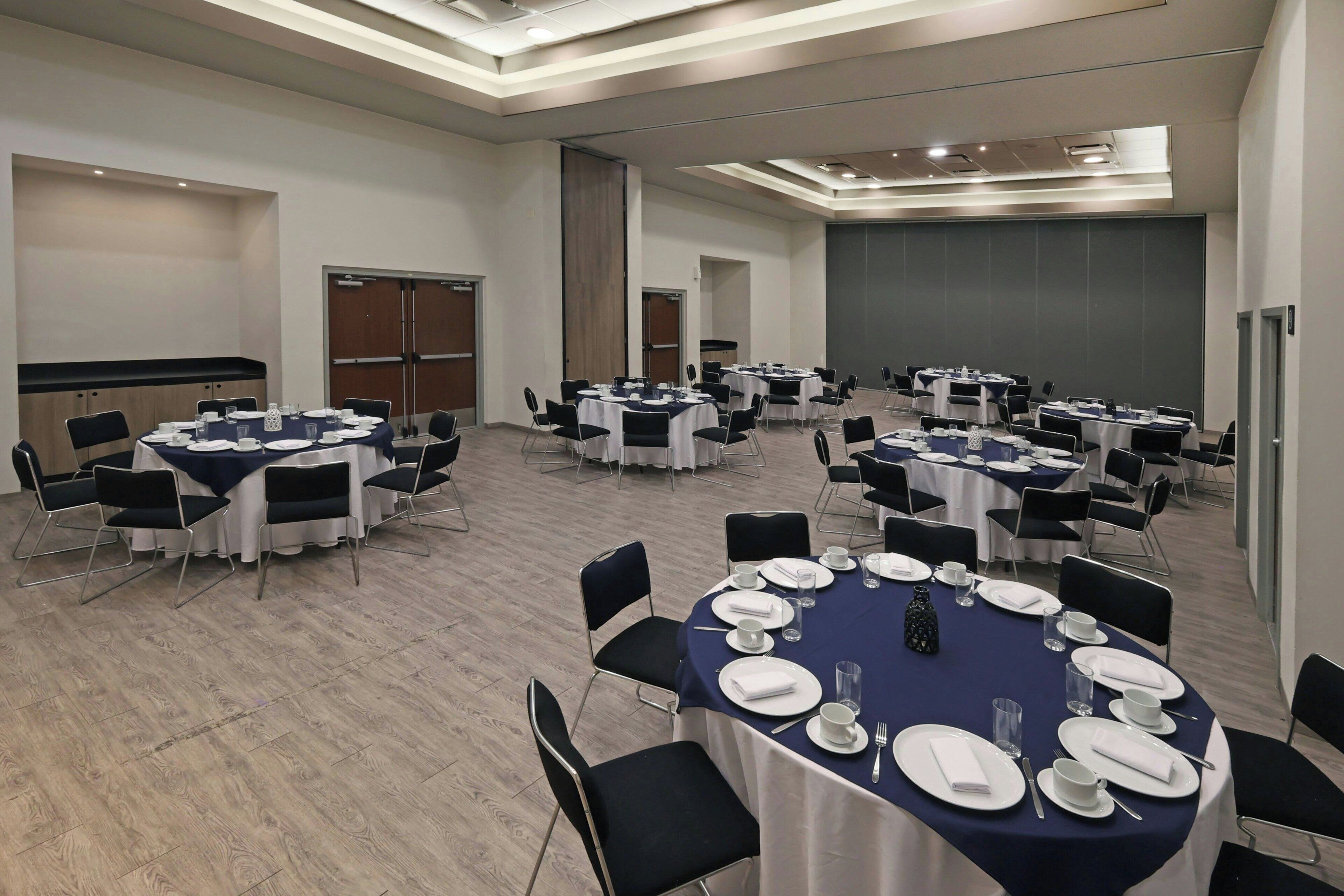 A conference room with multiple tables set for meetings, equipped with chairs and tables, and a large screen for presentations.