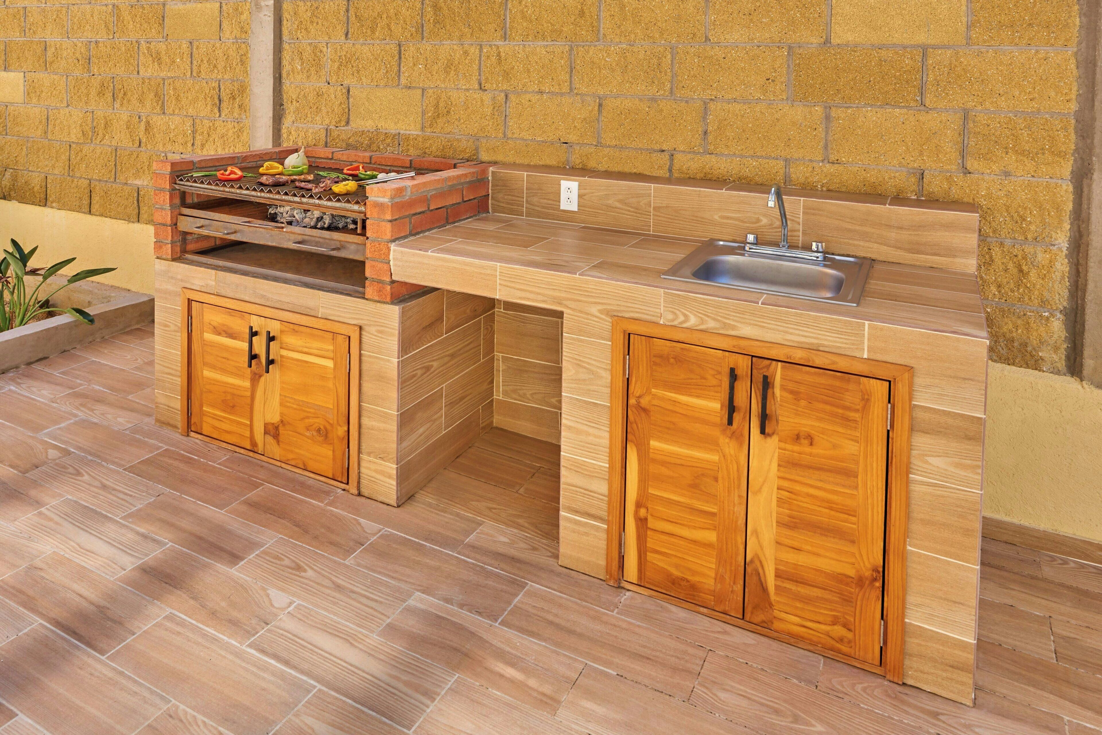 An outdoor kitchen with a brick grill, wooden cabinets, and a sink.