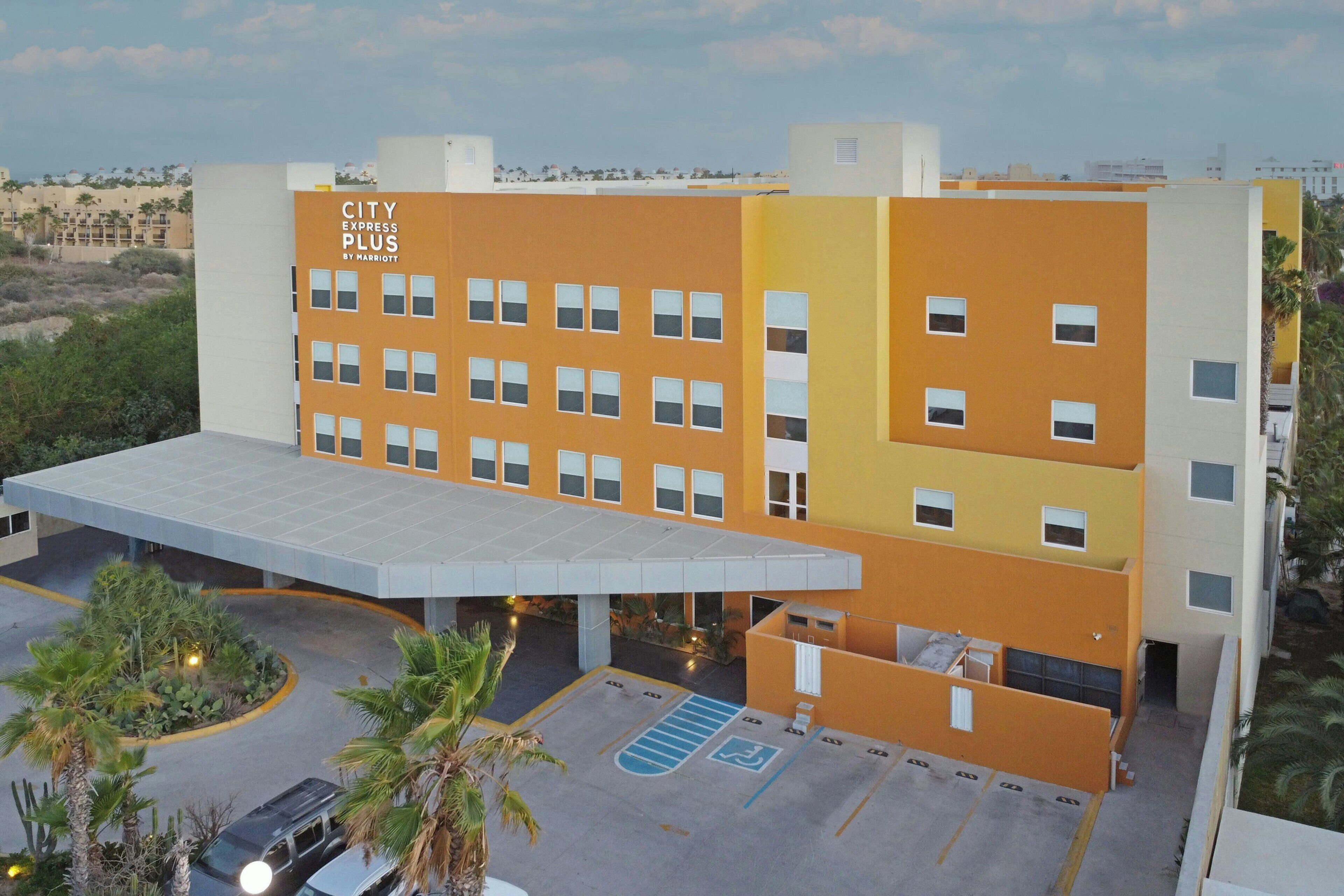 Un hôtel à plusieurs étages doté d’un toit plat, d’un parking couvert et d’une enseigne indiquant « CITY EXPRESS PLUS BY HARBORTON ».
