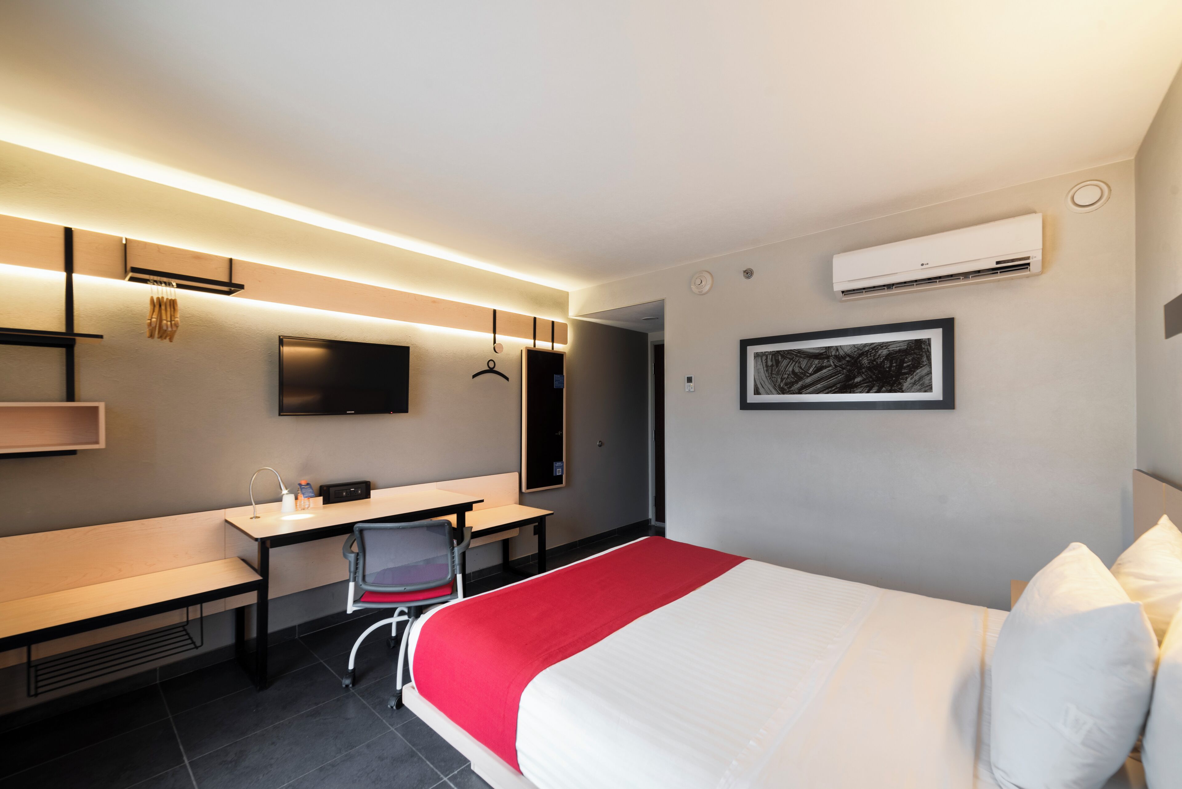 A modern hotel room with a bed, desk, chair, and a flat-screen TV mounted on the wall.