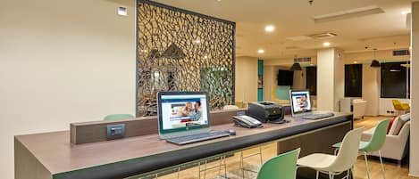 Balcão de recepção com computadores, telefone e área de estar com cadeiras.