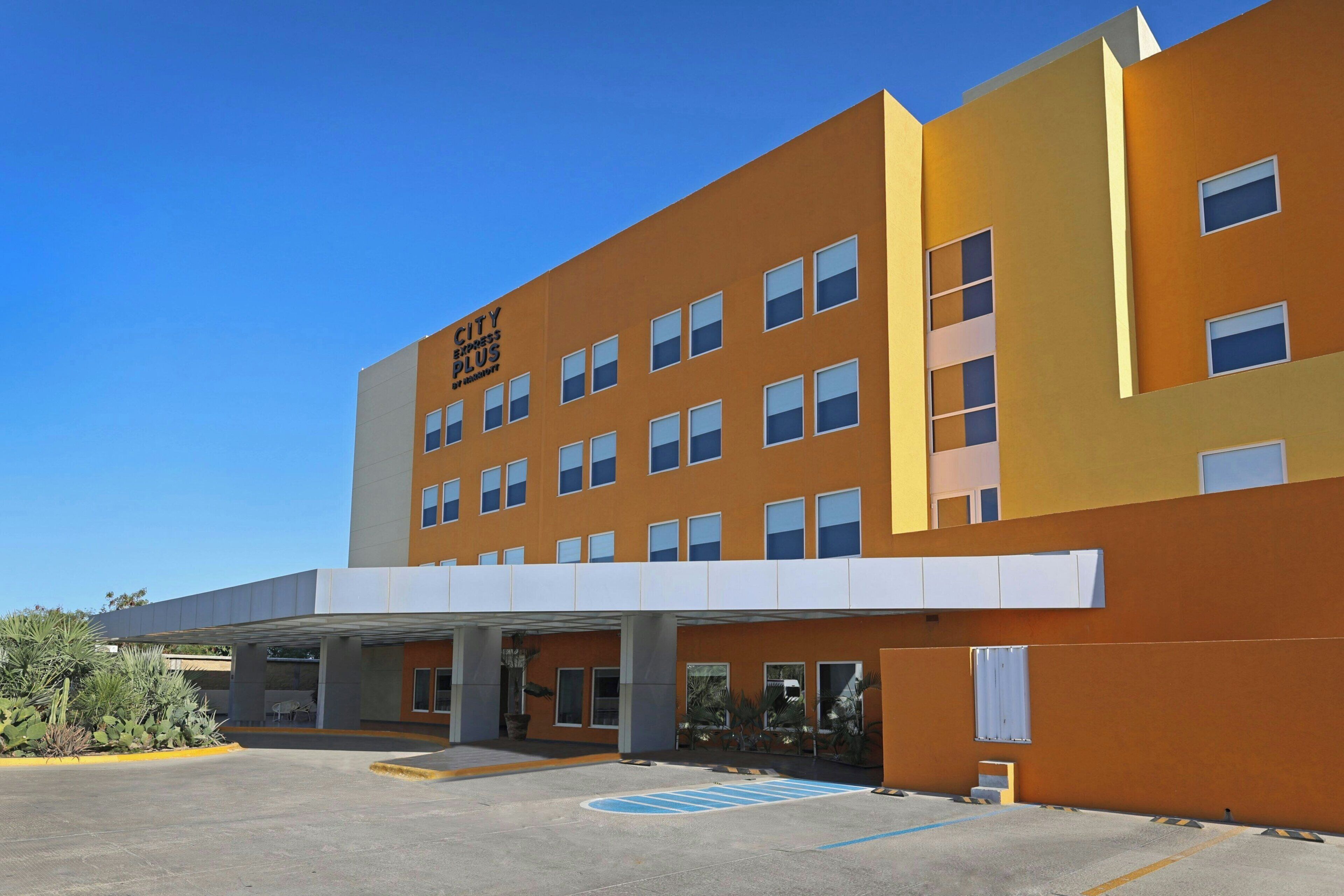 A modern hotel with a flat roof, multiple windows, and a covered entrance area.