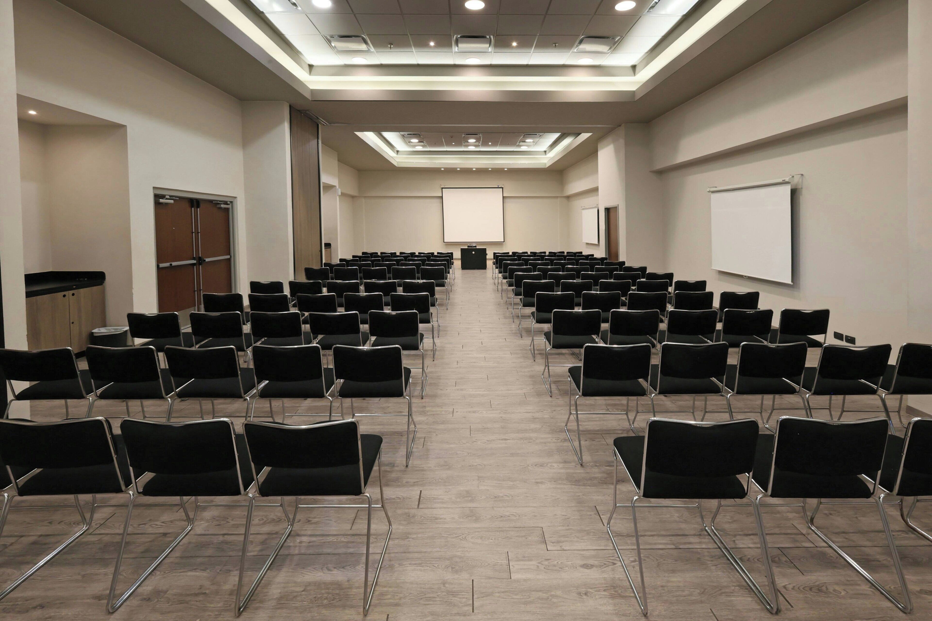 Une salle de conférence avec des rangées de chaises, un pupitre et un grand écran.
