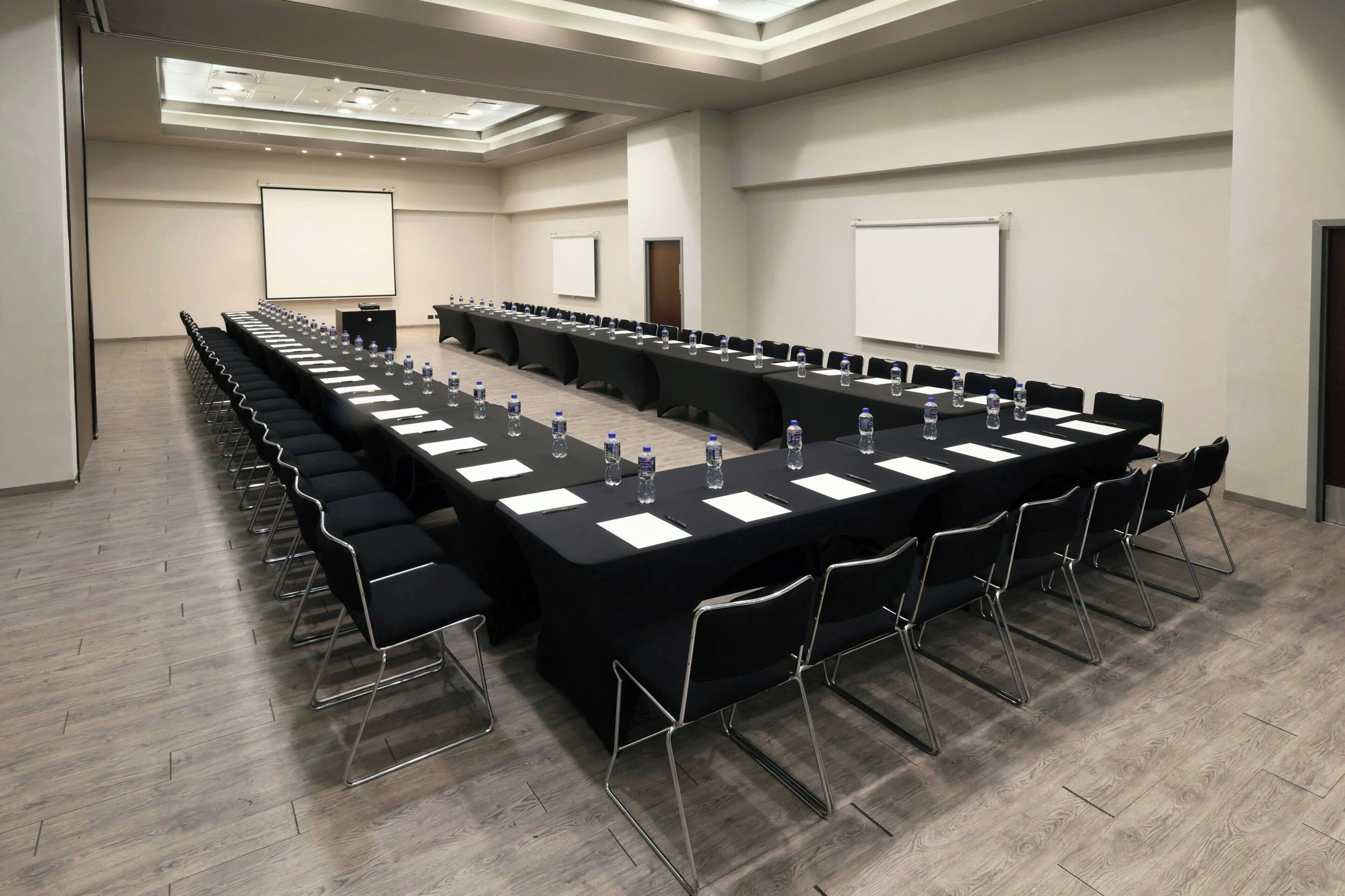 A conference room with a long table, chairs, water bottles, and a projector screen.