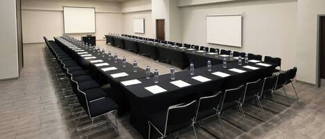 A conference room with a long table, chairs, water bottles, and a projector screen.
