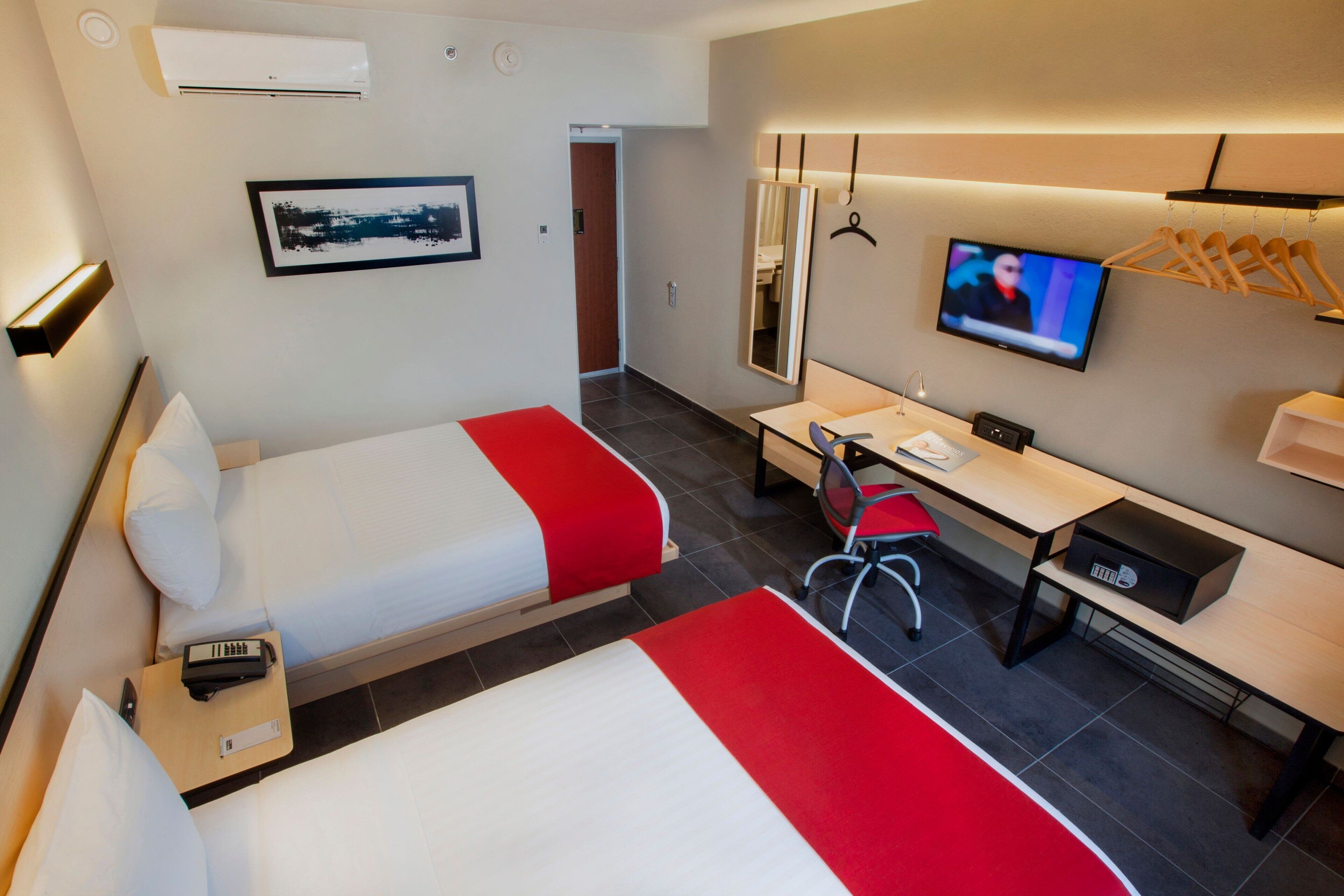 A hotel room with two beds, a desk, a chair, a TV, a mirror, and a wardrobe.