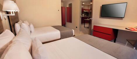 A hotel room with two beds, a desk, a TV, and a kitchenette.