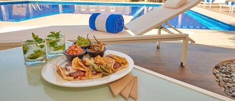 Una mesa junto a la piscina con comida, bebidas y una toalla enrollada.