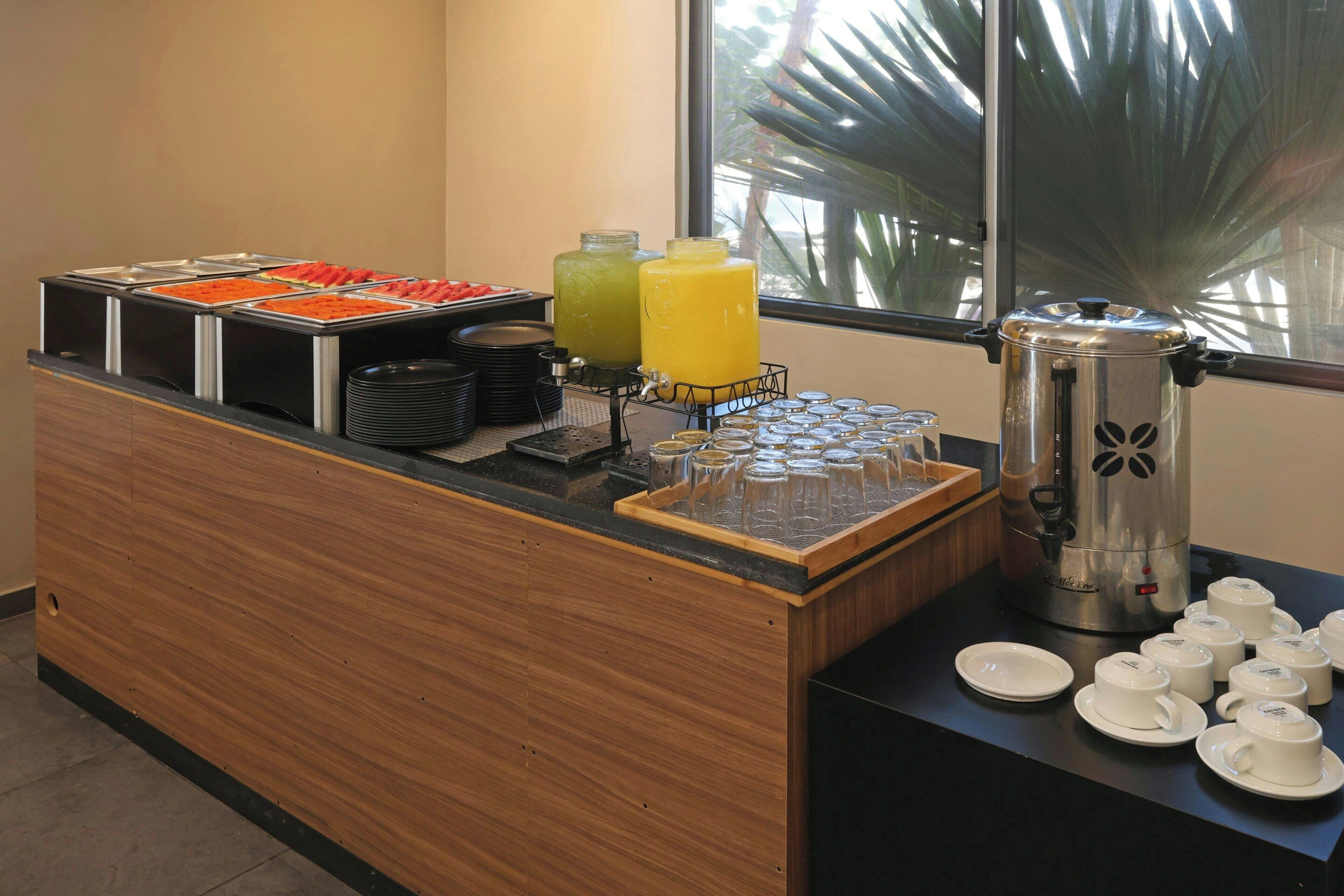 A buffet counter with various food items, a coffee maker, and a window with a view of palm trees.