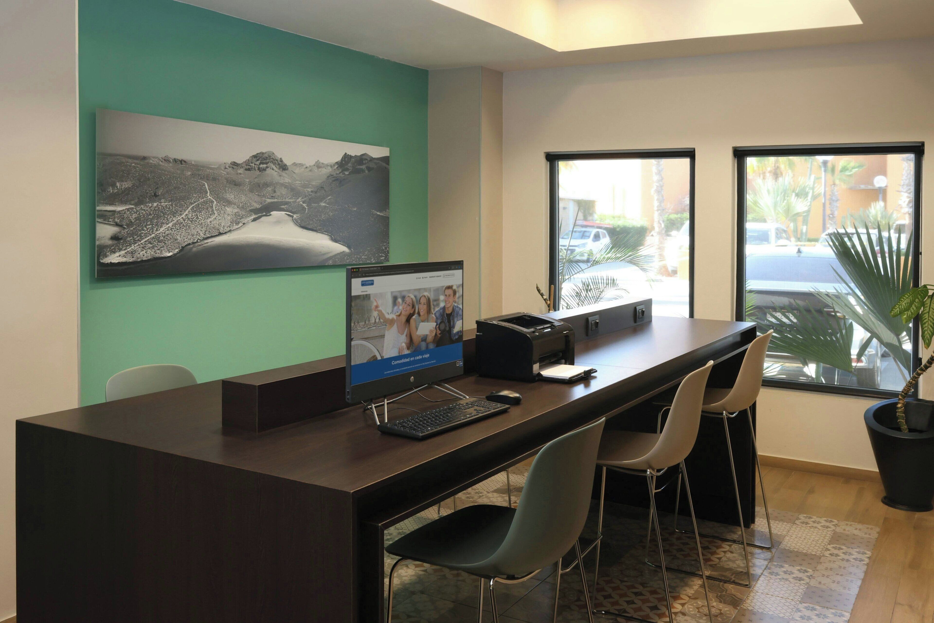 A reception desk with a computer, chairs, a printer, and a large window with a view of palm trees.