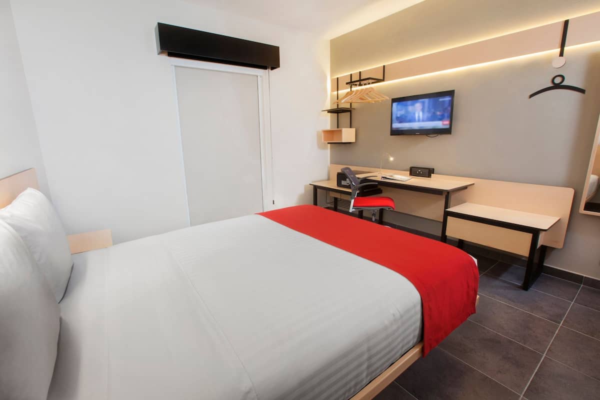 A hotel room with a bed, a desk, a chair, a television, and a wardrobe.
