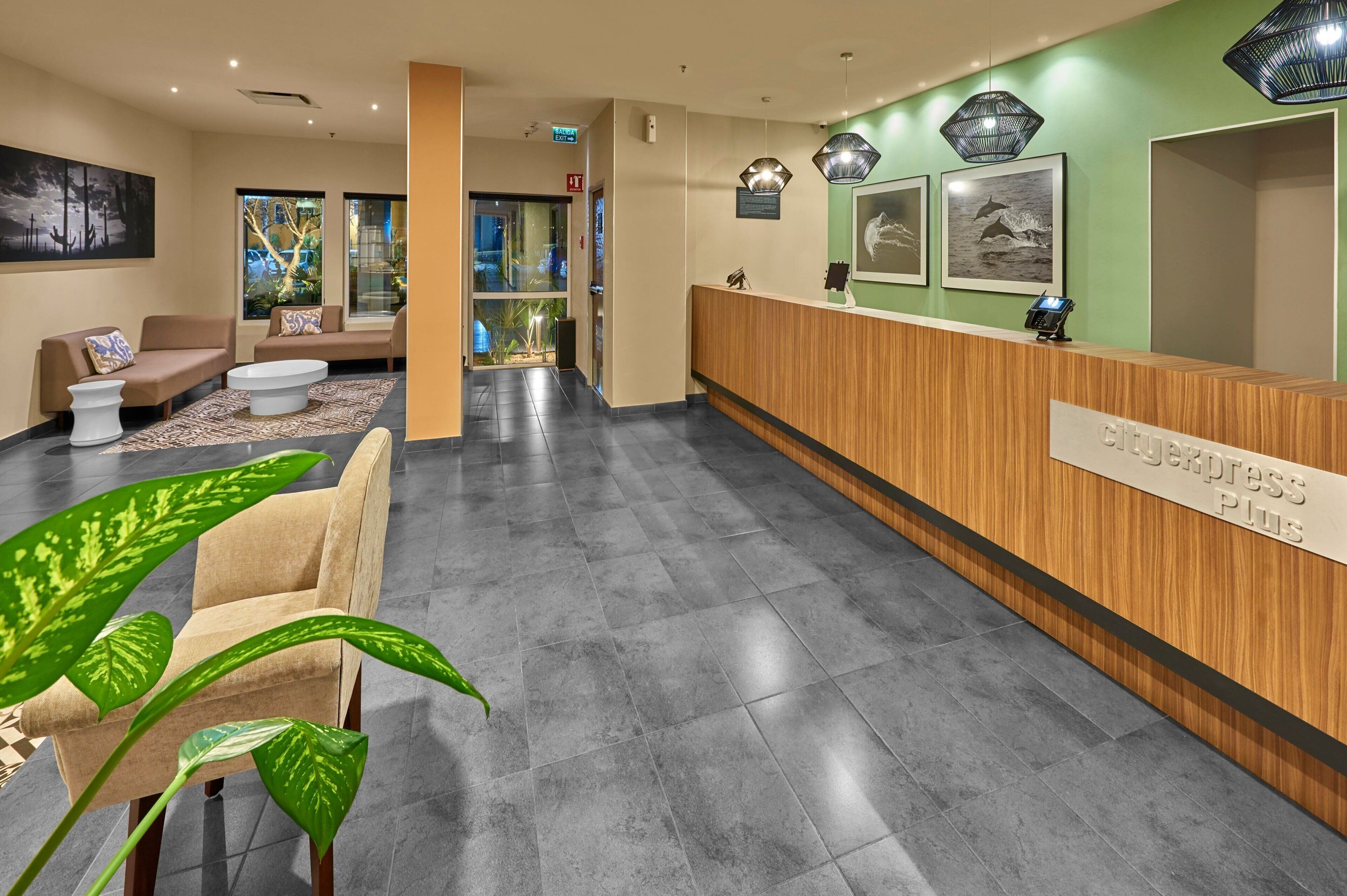 A reception area with a wooden reception desk, beige sofas, and a large green plant.