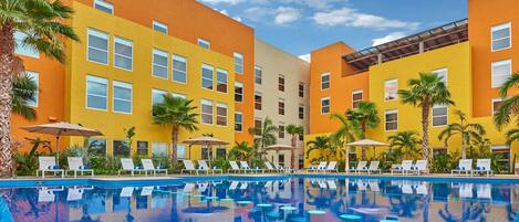 A hotel with a pool, multiple floors, and palm trees.