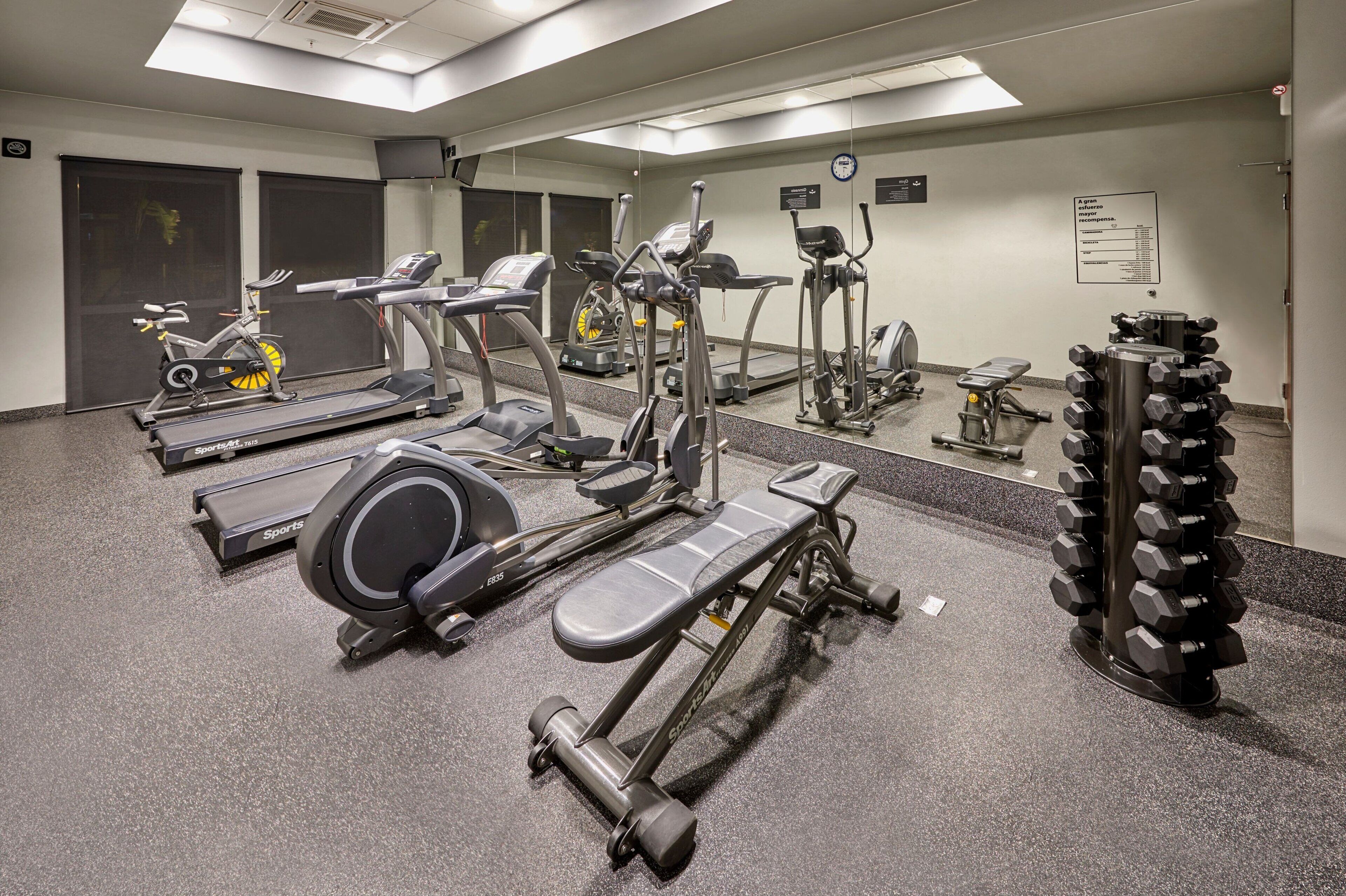 Une salle de sport équipée de divers appareils d’exercice, notamment des tapis de course, des vélos elliptiques et un banc de musculation.