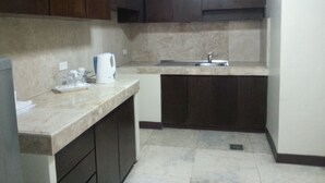 Una cocina con armarios de madera oscura, encimera de mármol, cafetera y fregadero.
