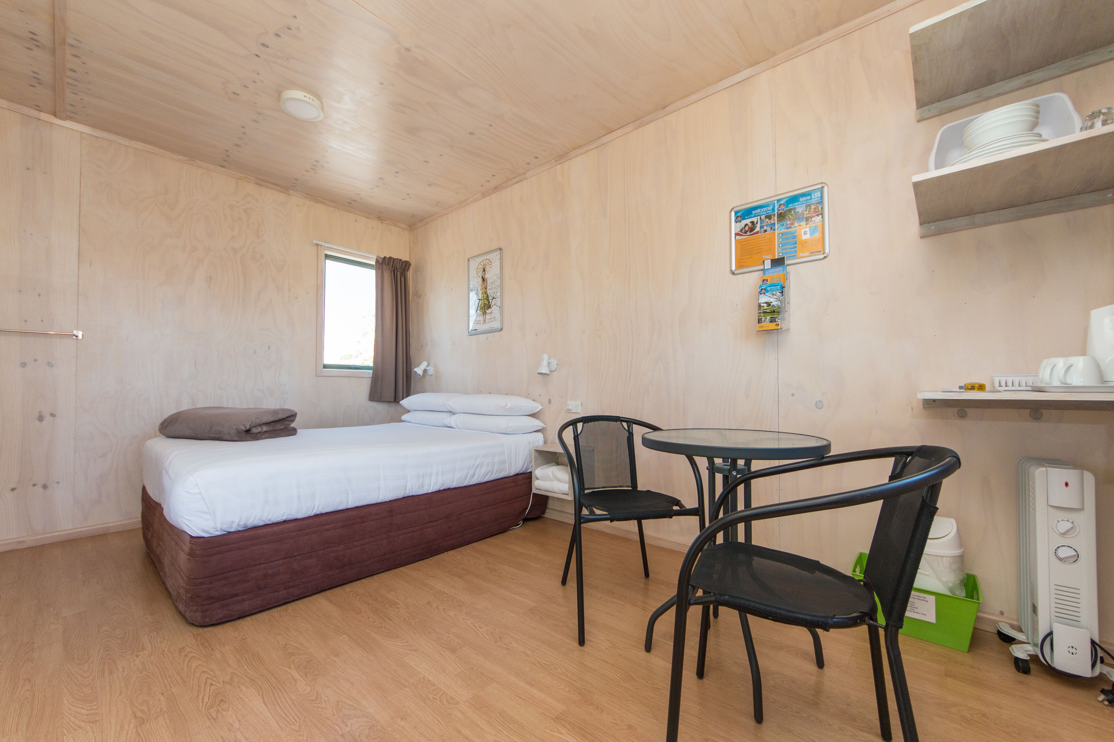 Una habitación con cama, una mesa con sillas, un escritorio con computadora y una estantería con platos.