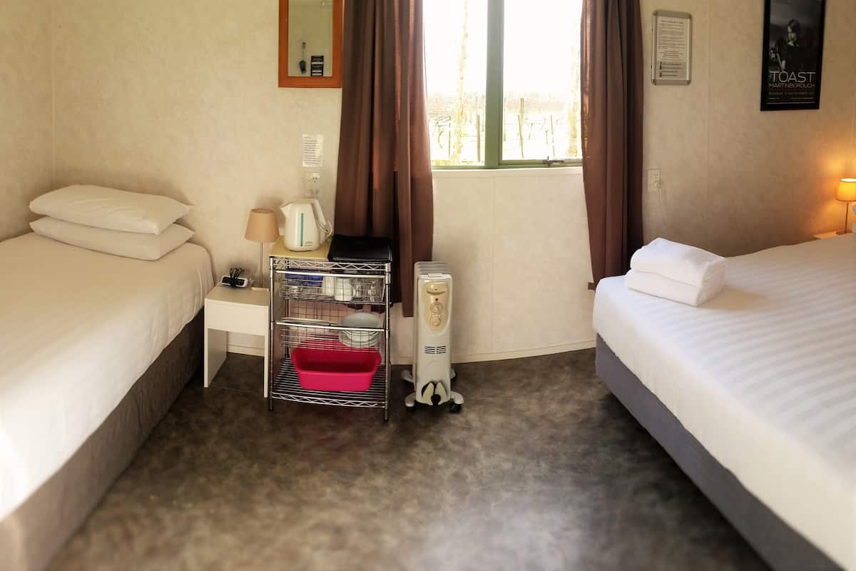 Ein Hotelzimmer mit zwei Betten, einem Schreibtisch mit Lampe, einer Kaffeemaschine, einem roten Korb und einem Heizgerät.