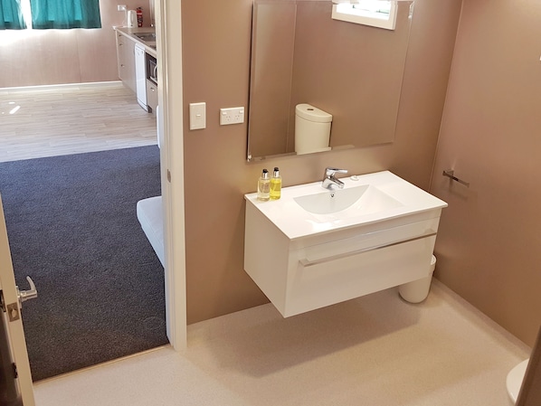 Un baño moderno con lavamanos, espejo e inodoro blancos.