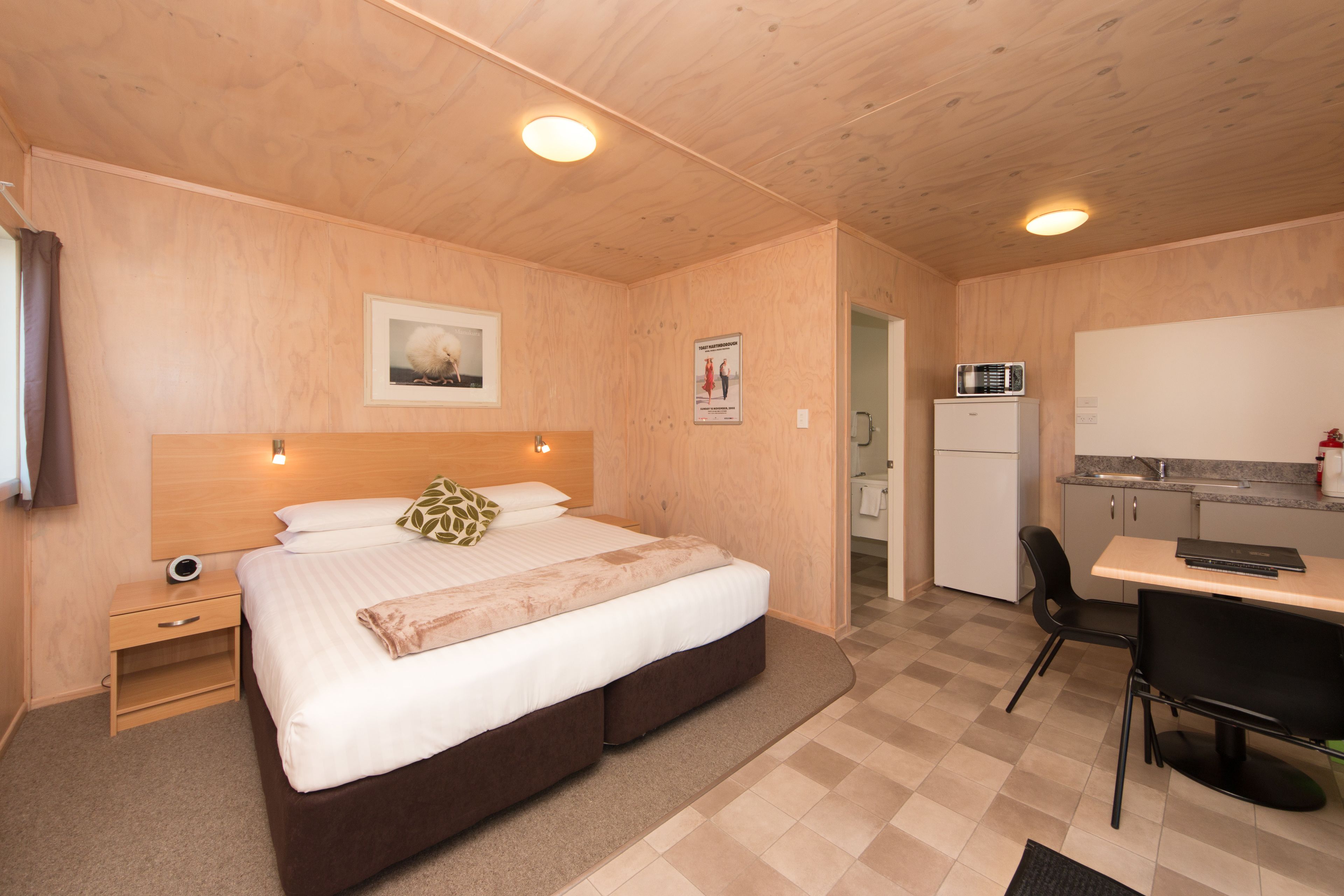 A room with a bed, bedside table, and a small kitchenette.