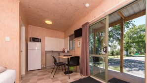 Una habitación funcional con cama, kitchenette, zona de comedor con mesa y sillas, y puerta corrediza de vidrio que da a un espacio exterior.