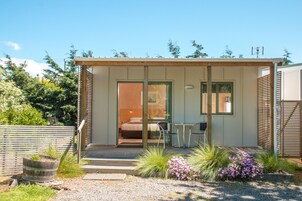 Una cabaña pequeña de una sola habitación con una cama, una mesa y sillas afuera.