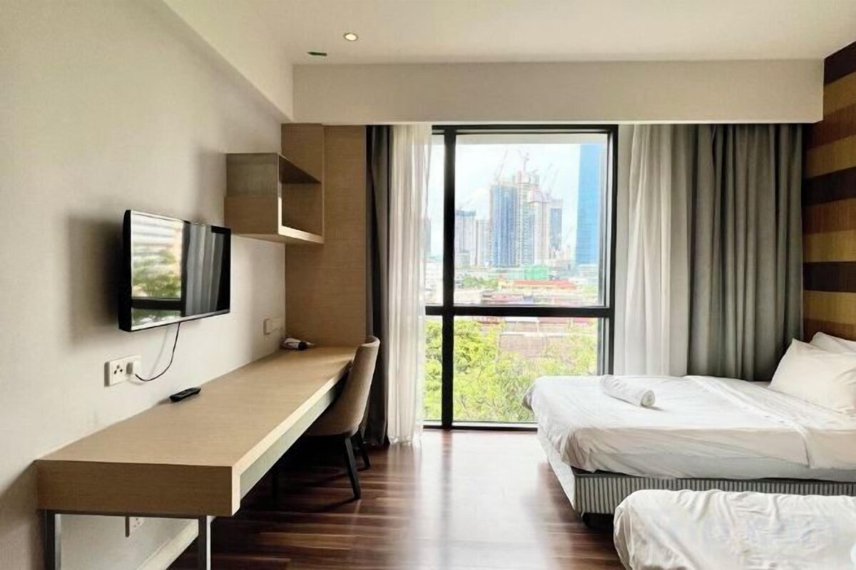 Une chambre d’hôtel comprenant un lit, un bureau avec une chaise, une télévision et une grande fenêtre donnant sur la ville.