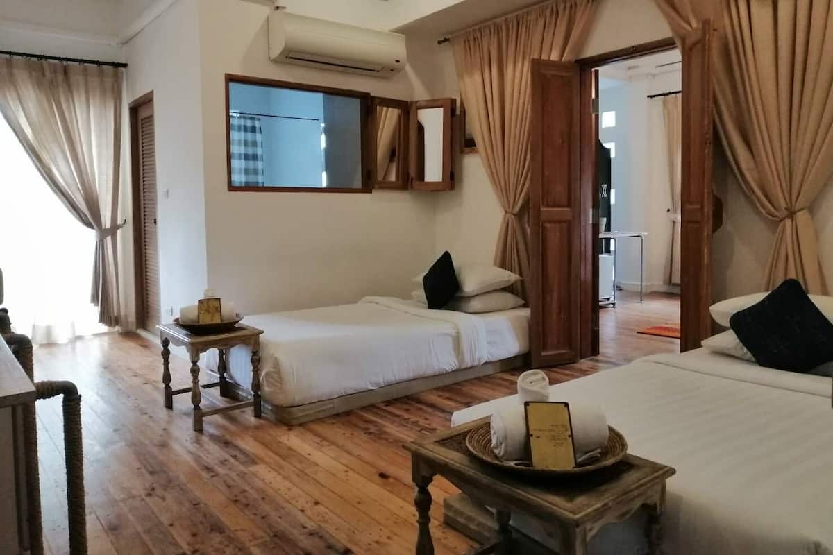 A hotel room with two beds, a wooden floor, an air conditioning unit, and a window with curtains.