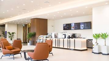 A modern lobby with seating, a reception area, and a coffee station.