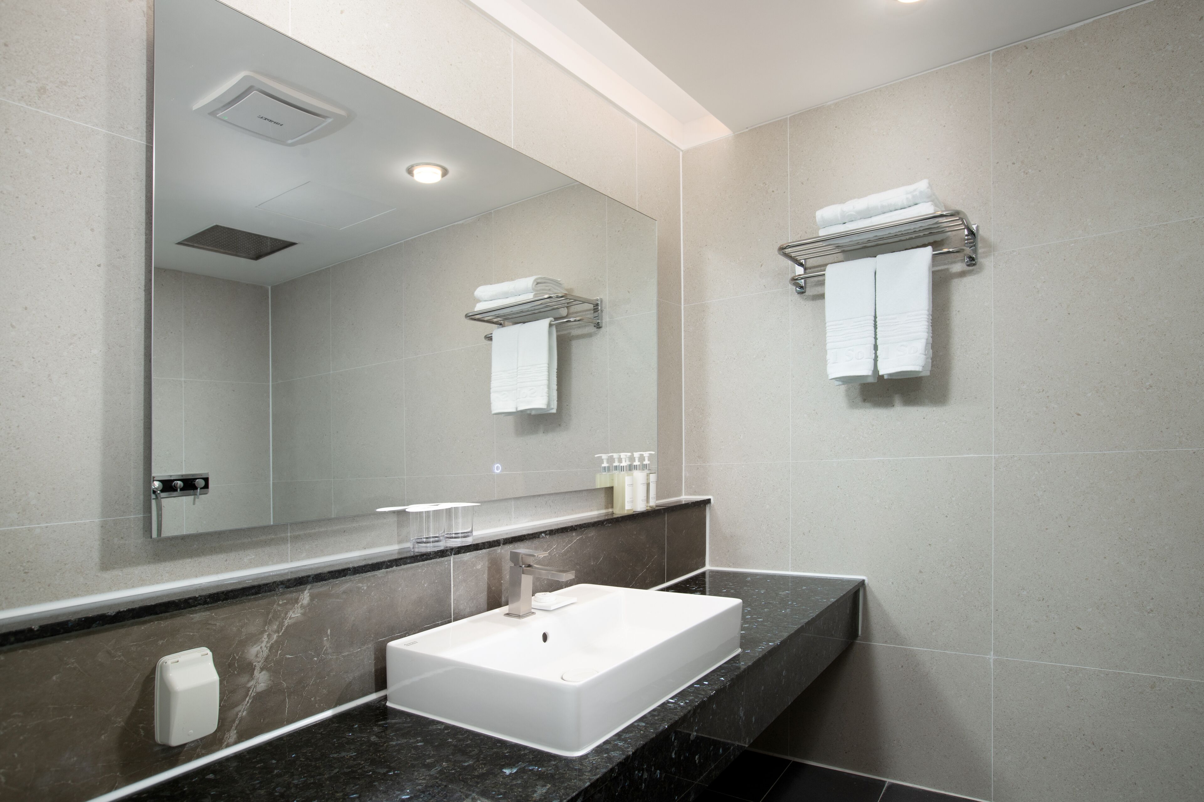 A modern bathroom with a large mirror, a white sink, and towel racks.