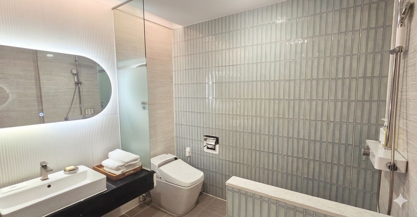 A modern bathroom with a large mirror, two sinks, a toilet, and a shower area.
