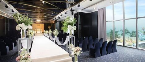 Un salón de conferencias con filas de sillas, una mesa larga y centros de mesa con flores.