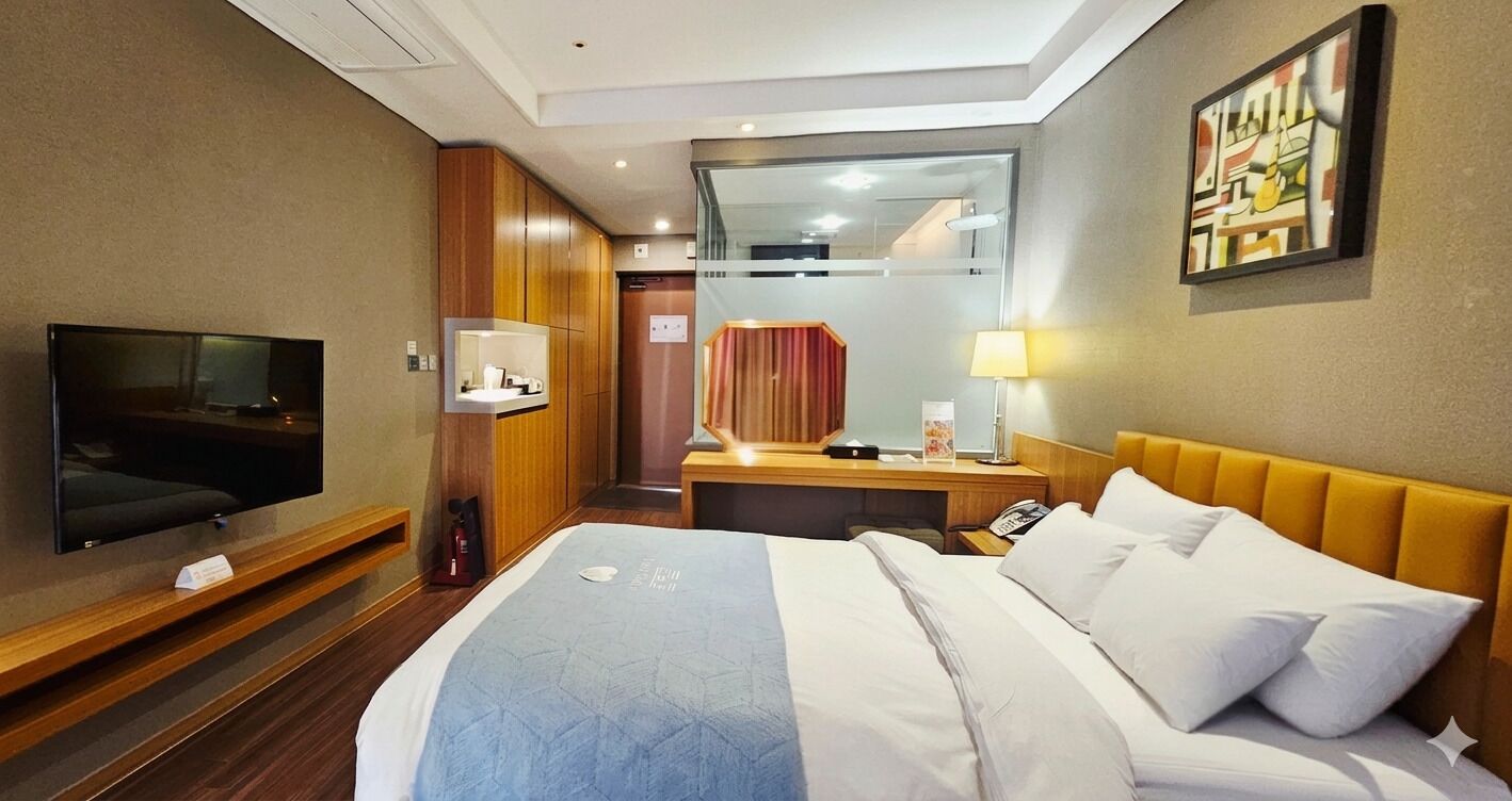 A hotel room with a bed, a TV, a desk with a lamp, a mirror, and a painting on the wall.
