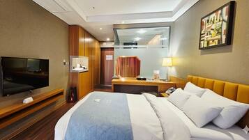 A hotel room with a bed, a TV, a desk with a lamp, a mirror, and a painting on the wall.