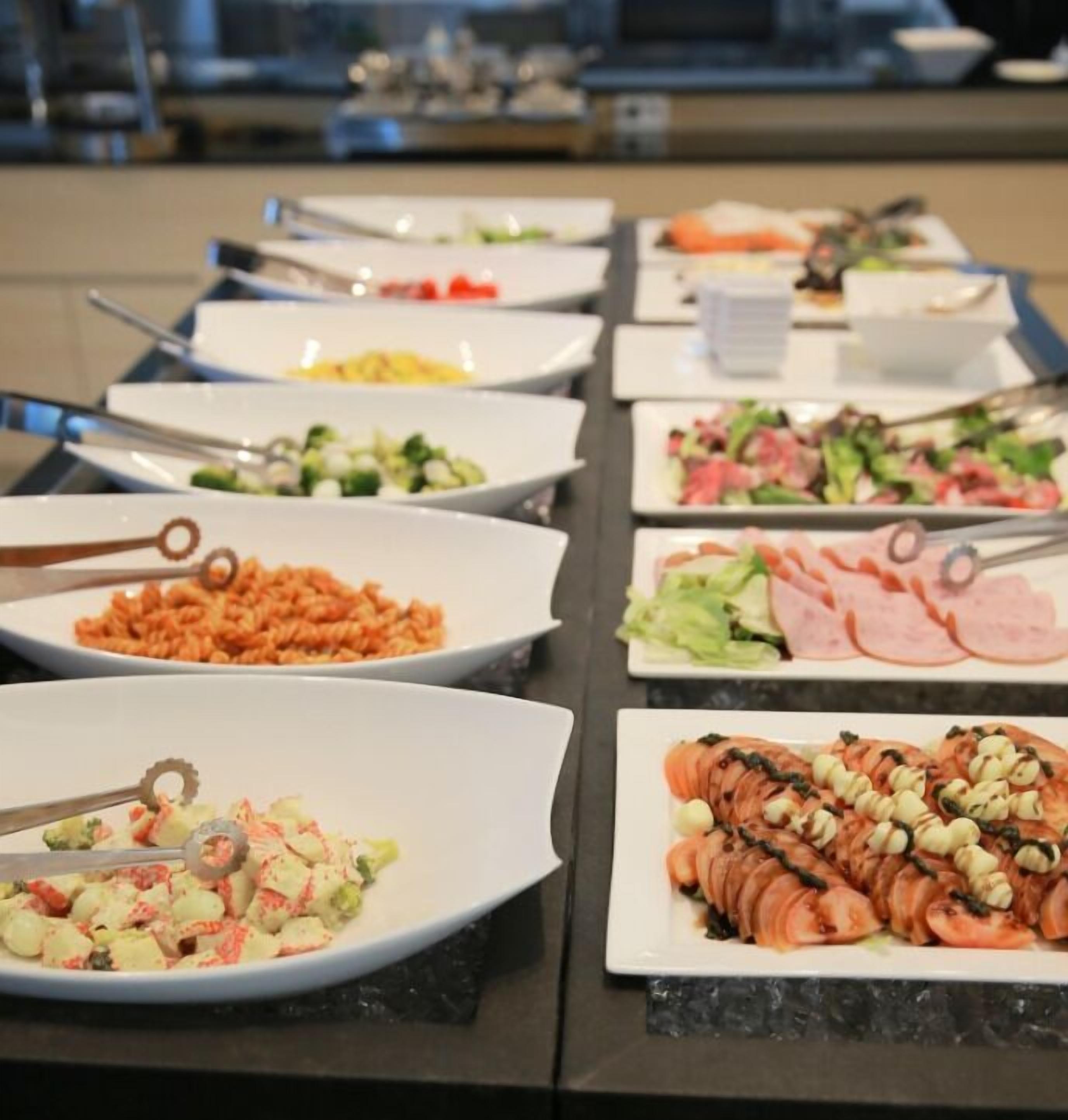 Un bufé con diversos platos, entre ellos pasta, ensaladas y fiambres.