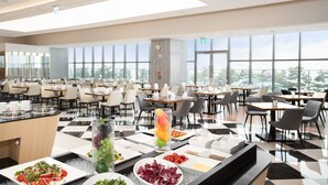 Un'ampia sala da pranzo con numerosi tavoli e sedie, un'area buffet con diverse pietanze e ampie finestre che offrono vista sull'esterno.