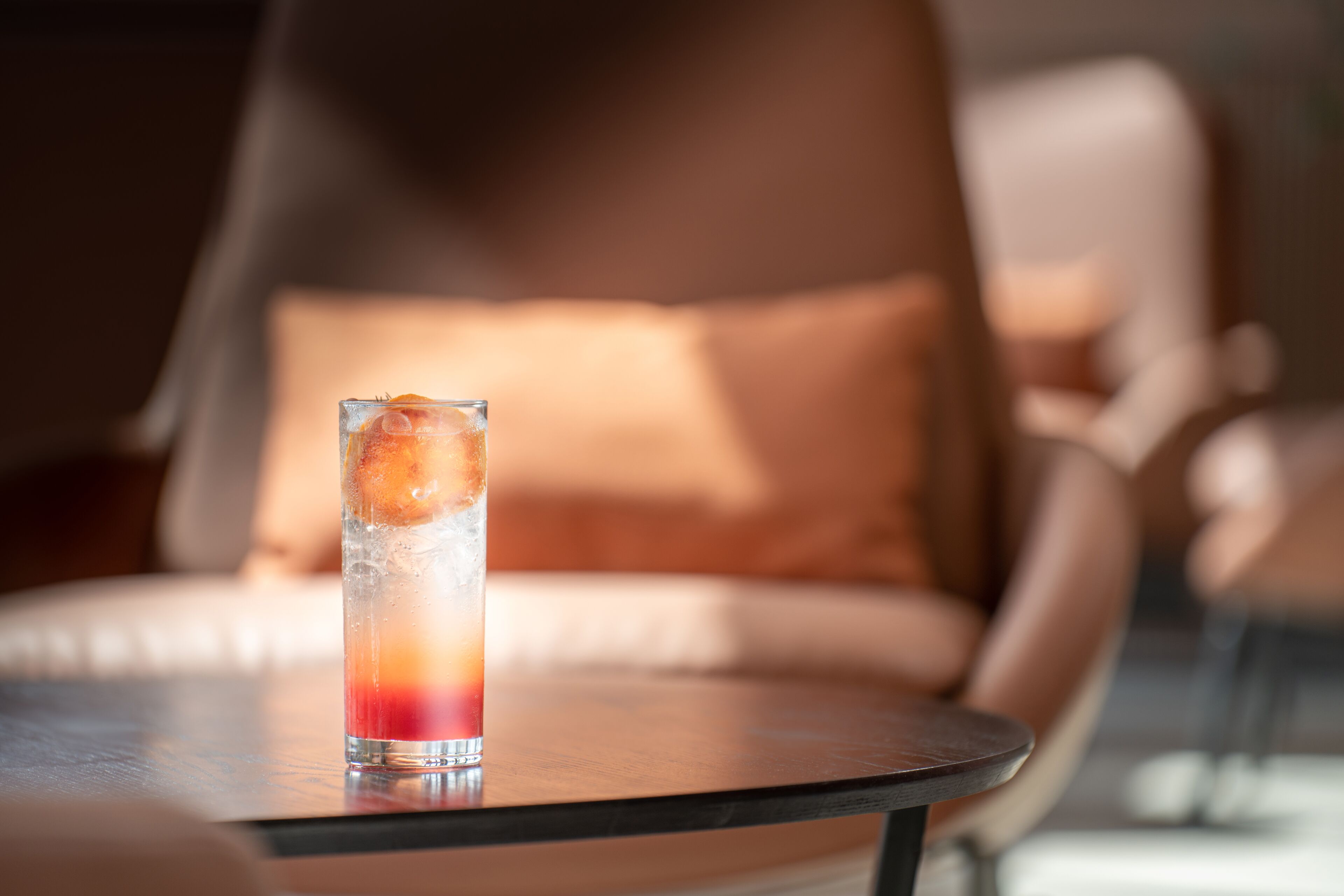A glass of red and orange drink on a round table with a chair in the background.