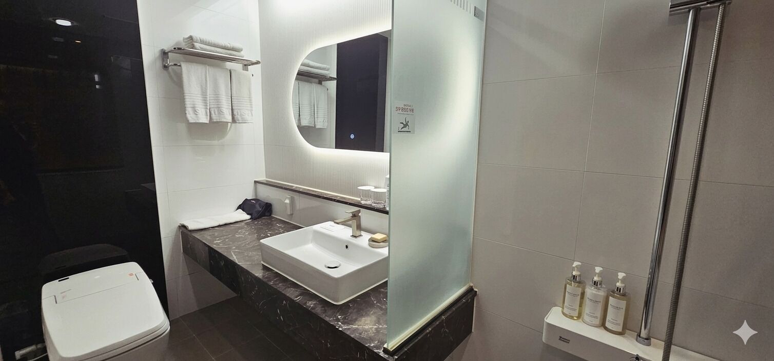 Un baño moderno con un lavamanos blanco, un espejo, toallero y zona de ducha.