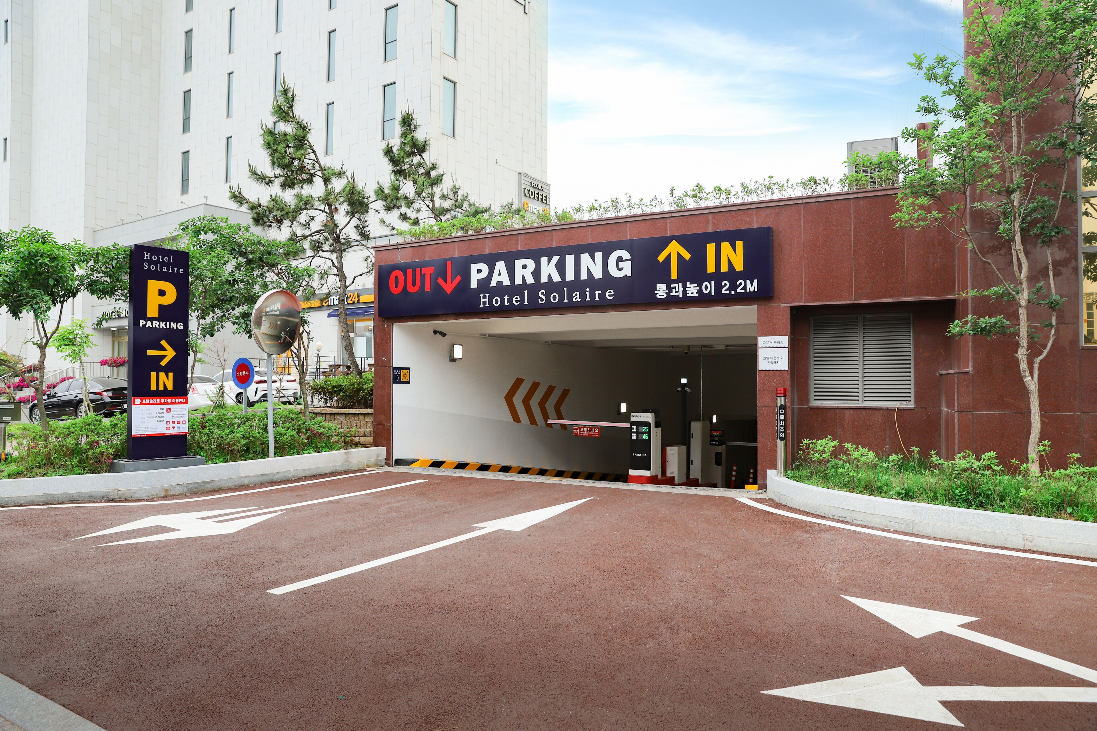 Entrada de hotel con señalización clara indicando la dirección hacia el estacionamiento y una fachada de edificio moderna.