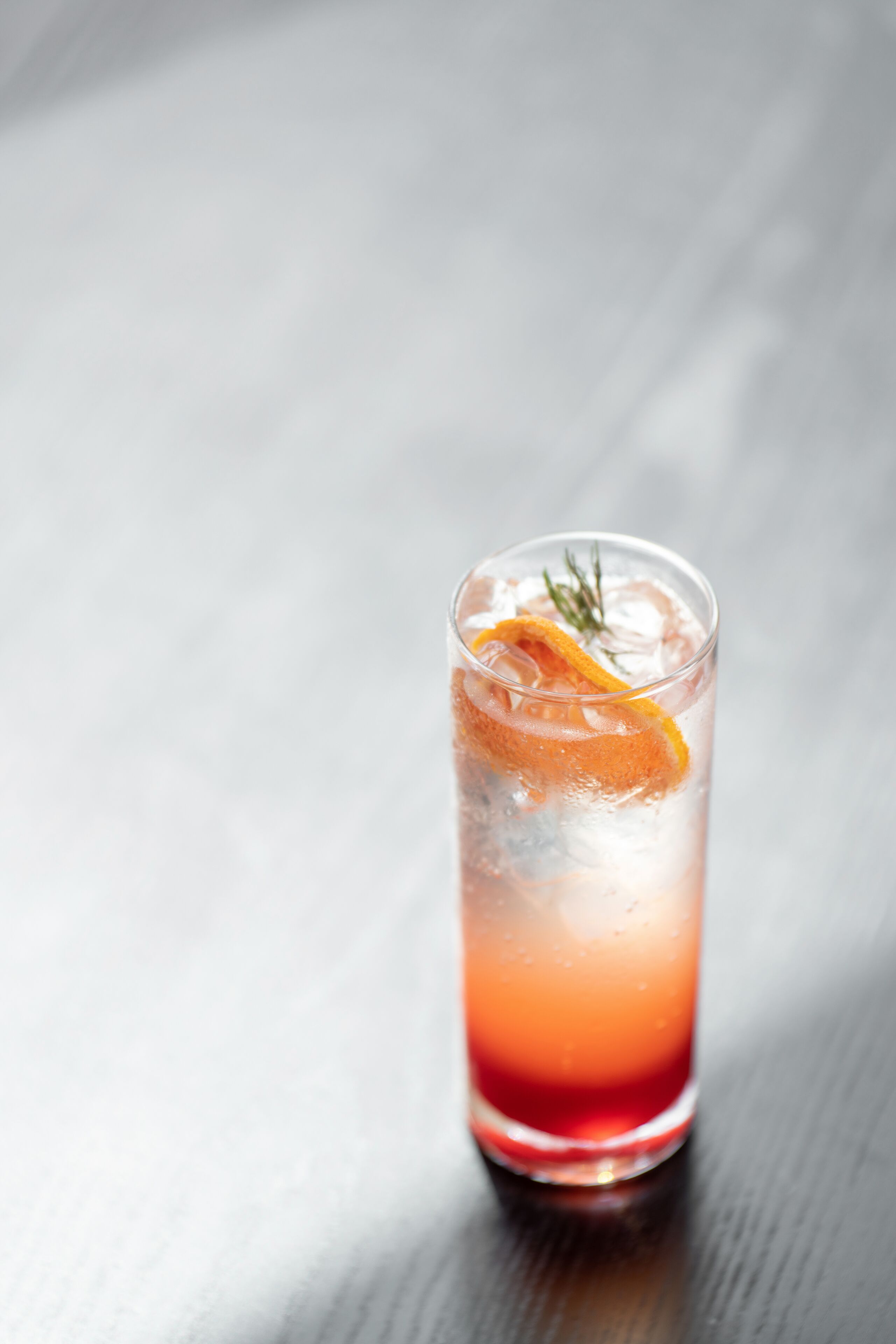 A tall glass with a gradient drink, ice, and a slice of orange on a wooden surface.