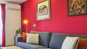 Un salon moderne avec un mur d’accent rouge, un canapé gris agrémenté de coussins à motifs, une table basse en bois et un tableau encadré.