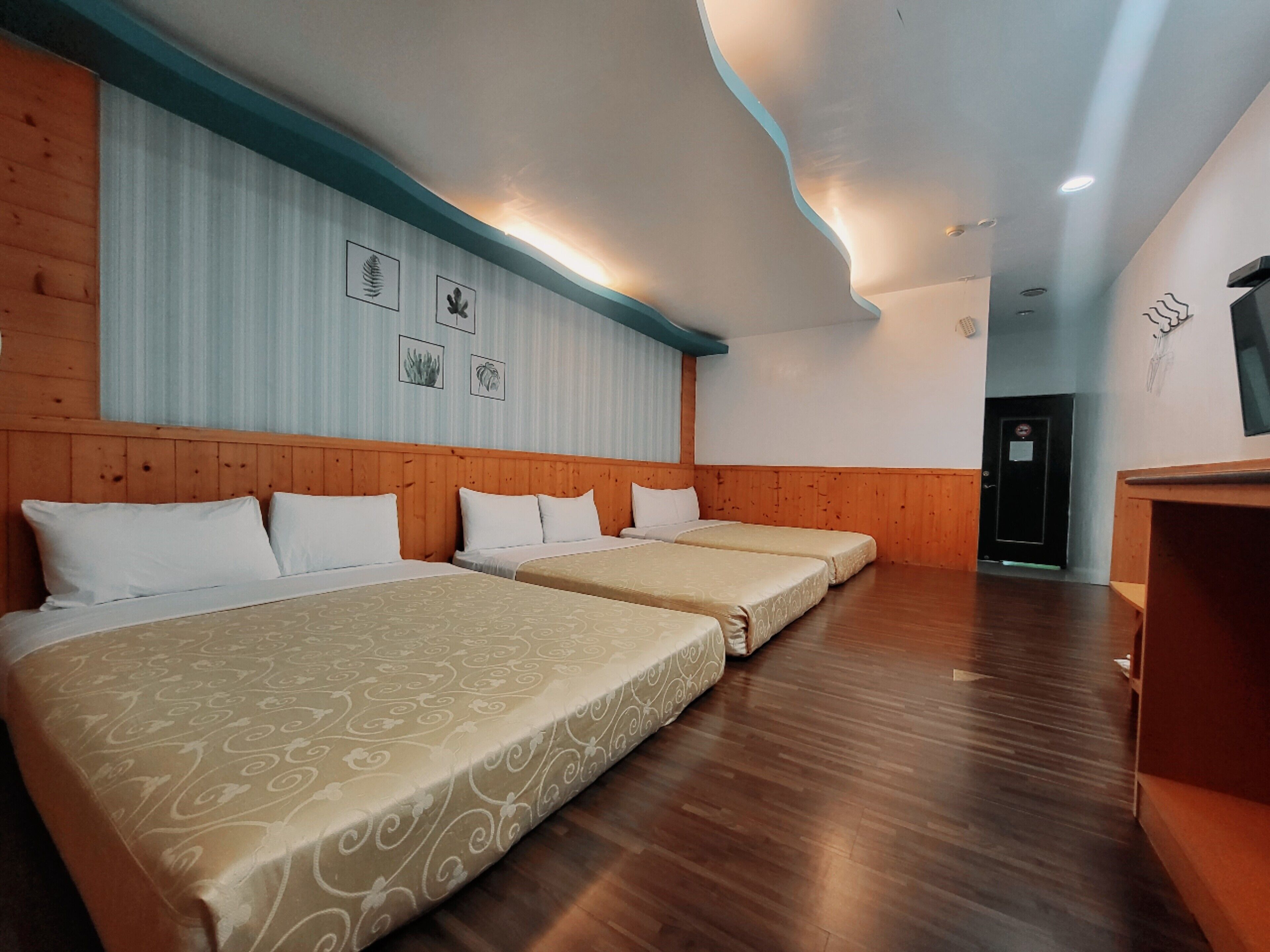 Habitación de hotel con tres camas, cabeceras de madera, suelo de madera y una pared decorada con cuadros.