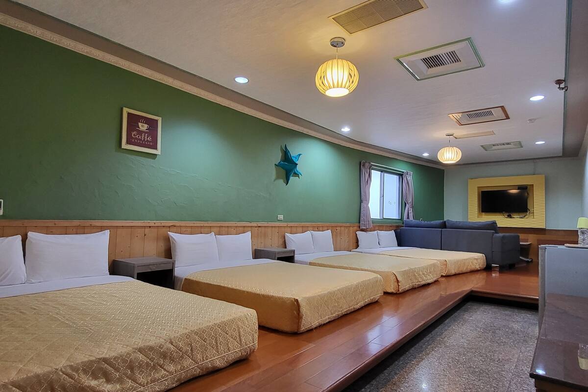 Quarto de hotel com três camas, uma televisão e um detalhe decorativo em formato de estrela na parede.