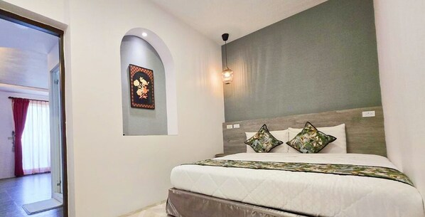 A bedroom with a bed, a nightstand, a wall-mounted light, and a door leading to another room.