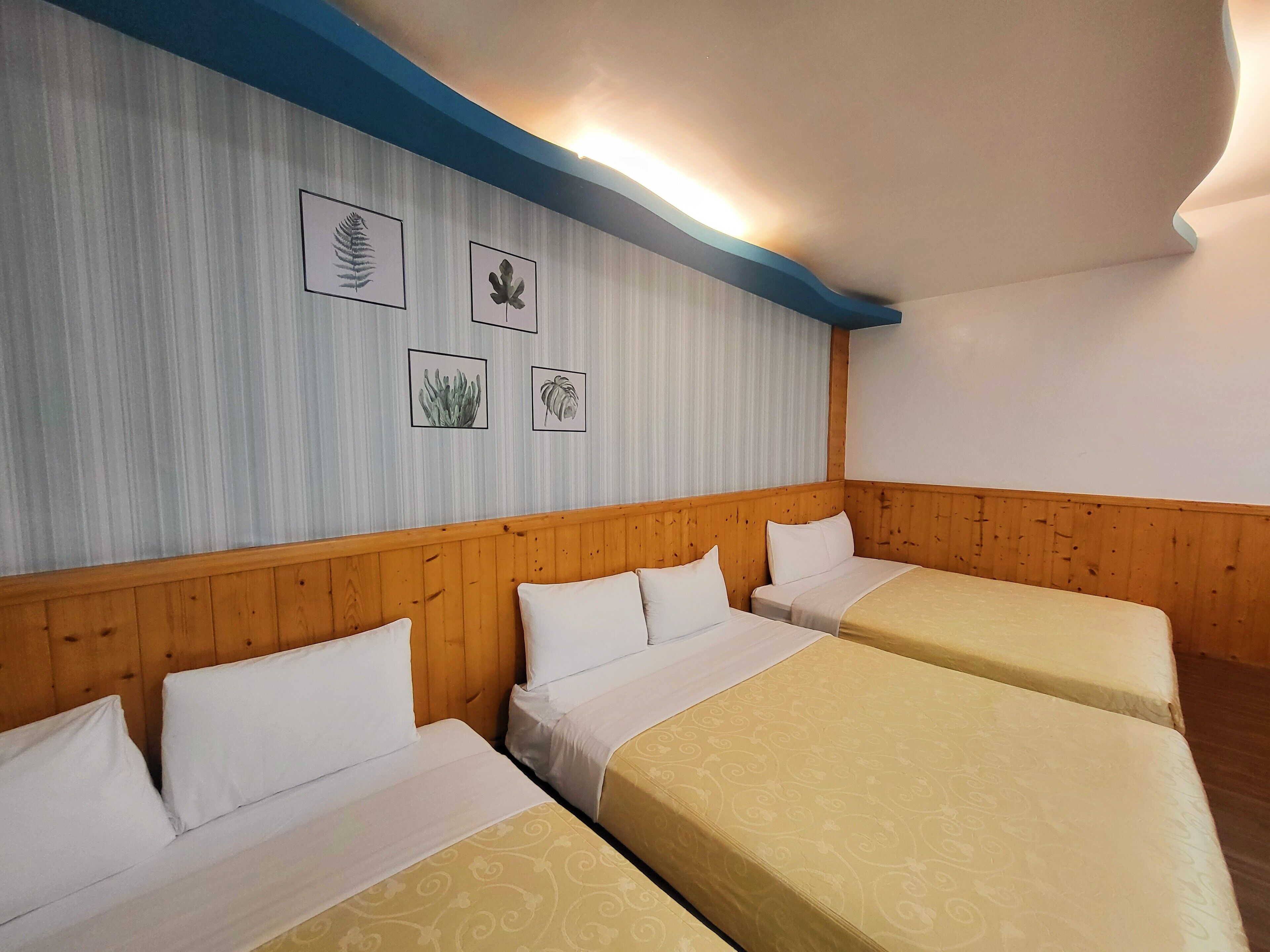 Habitación de hotel con tres camas, cabecero de madera y pared decorada con ilustraciones botánicas enmarcadas.