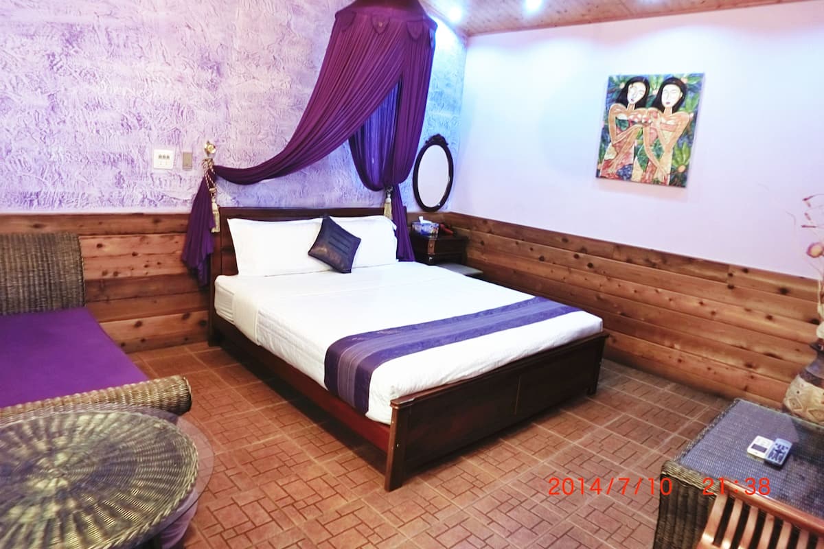 A bedroom with a wooden headboard, a canopy bed, a small bedside table, a chair, and a painting on the wall.